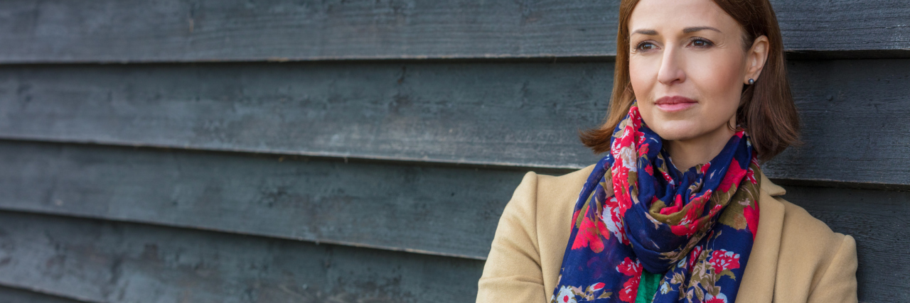 Why Those With Chronic Illness Shouldn't Say, 'If Only...' woman wearing a pink and blue scarf standing outside against a gray wall