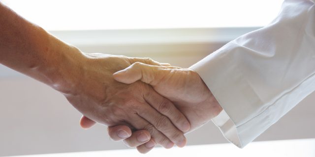 A photo of a male doctor's hand shaking another man's hand.