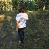 Back of girl, she is wearing a white shirt and jeans, walking in the woods