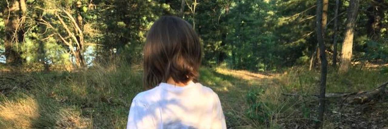 My Daughter Needs Me to Be Her Parent, Not Her Educator Back of girl, she is wearing a white shirt and jeans, walking in the woods