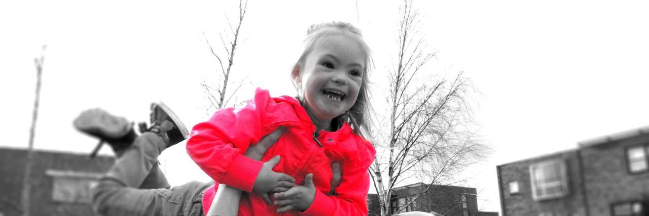 Dad Raps Song for Daughter With Down Syndrome Black and white image of dad lifting daughter ith Down syndrome in the sky, her coat is red, only color in the image