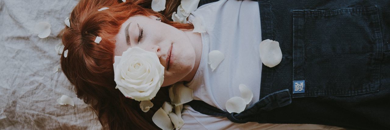 woman with tattoos laying on bed with flowers around her