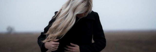 blonde woman wearing black coat and looking away from camera