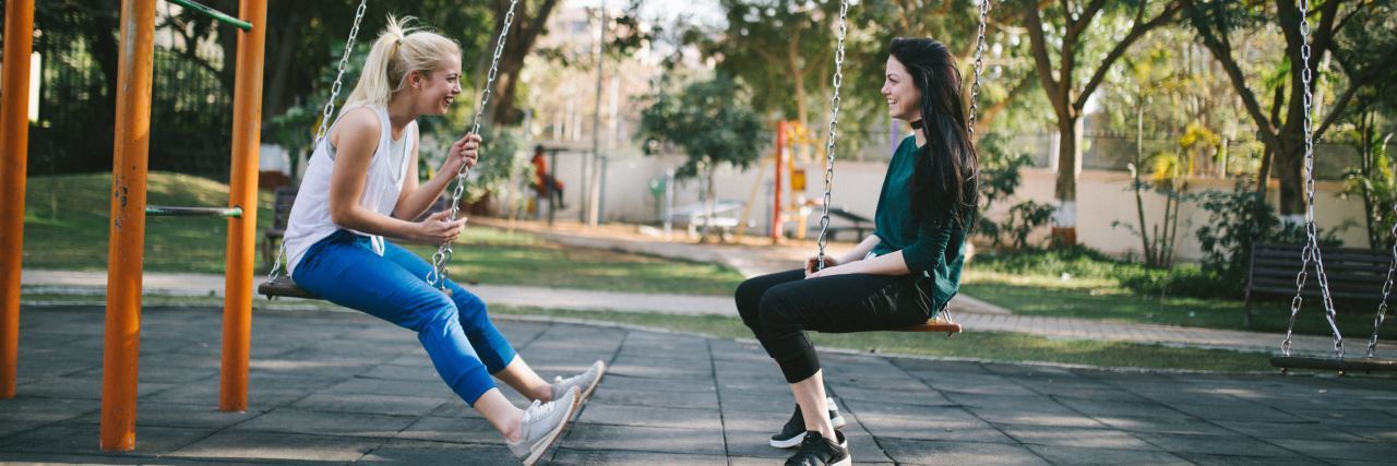 two women sitting on swings and talking