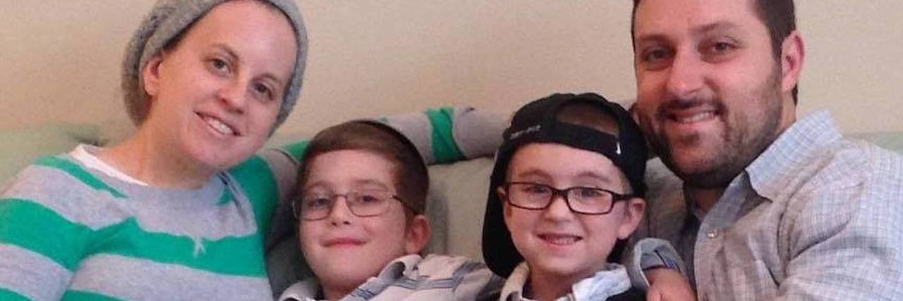 Making the Choice to Stay Home After My Child's Diagnosis Mom, two children, then dad sitting on a couch close together and smiling at camera