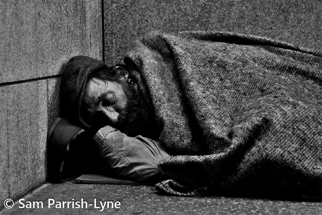 Homeless man lying on the street, photo by Sam Parrish-Lyne.