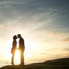 couple silhouetted against sunset with woman on tip toes to kiss man