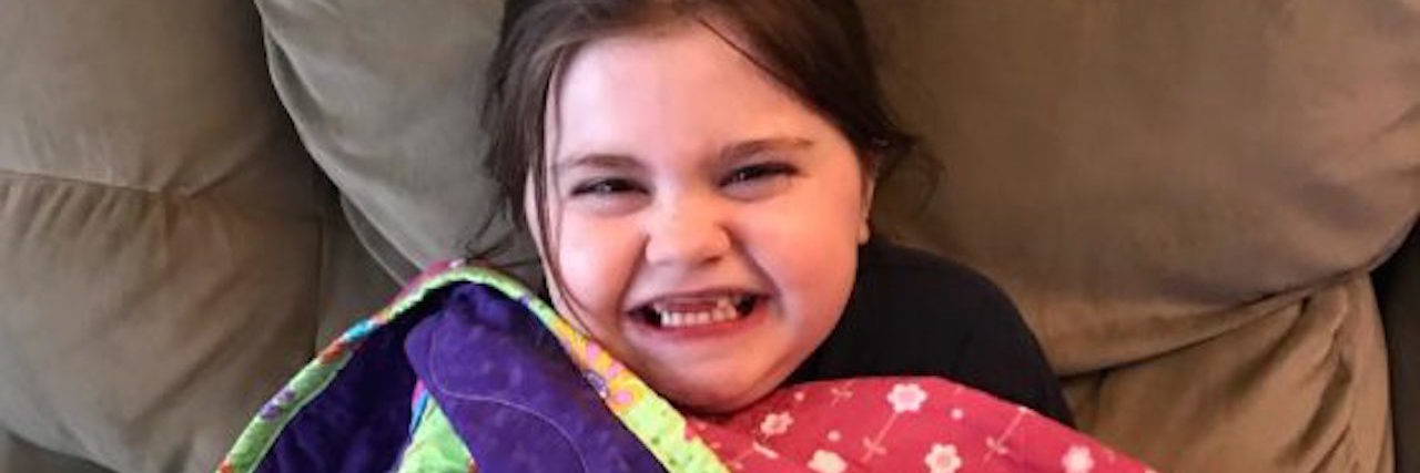 Making Quilts for Children With Juvenile Myositis young girl smiling with quilt