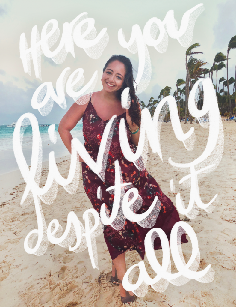woman wearing a dress and smiling on the beach with the words 'here you are living despite it all'
