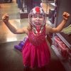 Little girl wearing a fancy pink dress and a football helmet, showing her muscles and making a "fierce" face