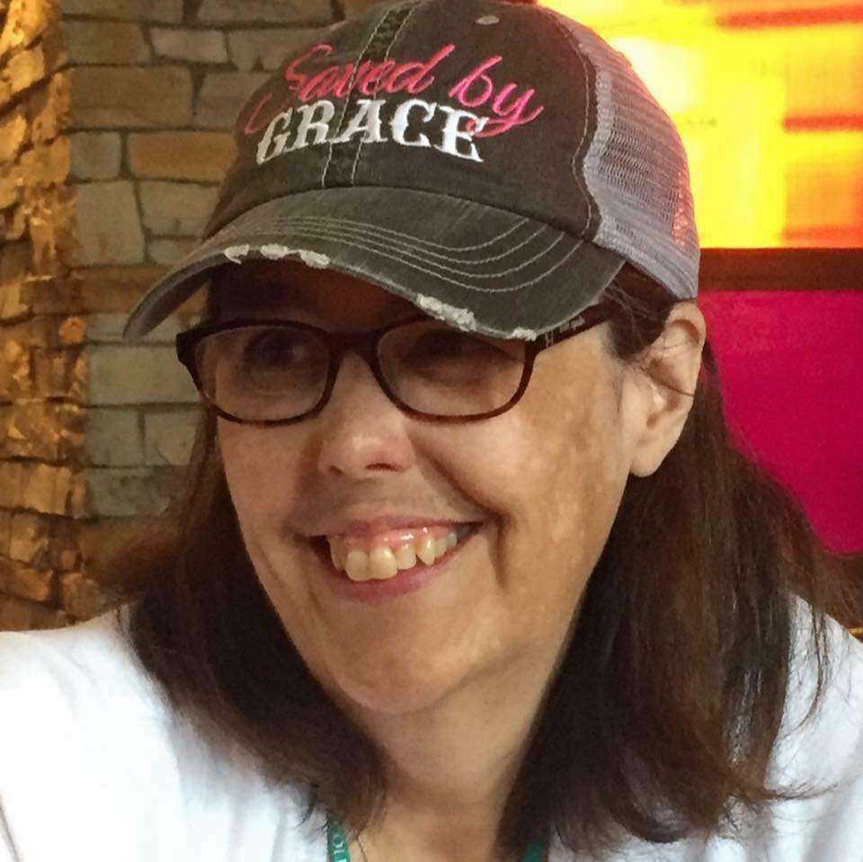 woman wearing glasses and a baseball cap. she has various colors of pigment on her skin