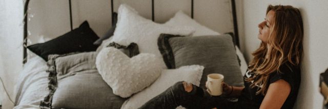 tired woman sitting on bed with cup of coffee