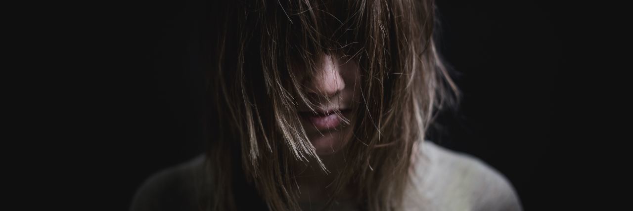 The 'Harmless' Jokes That Hurt My Mental Health young woman in darkness with hair covering eyes looking down