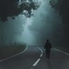 man walking along road in thick fog bordered by trees