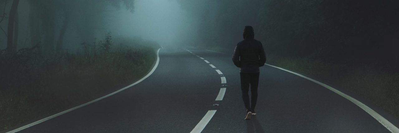 man walking along road in thick fog bordered by trees