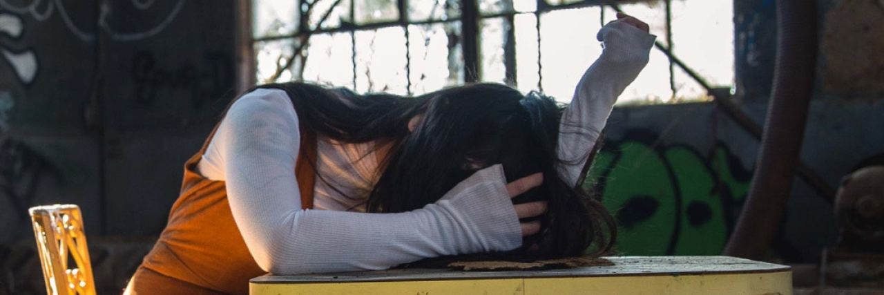 An Introduction to Life With Borderline Personality Disorder young woman in abandoned building resting head and arms on wooden table