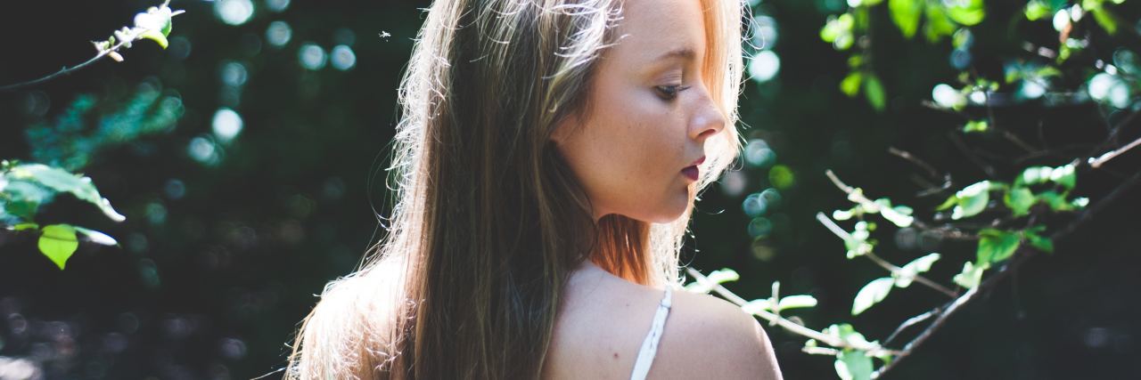 young woman in front of trees looking over shoulder