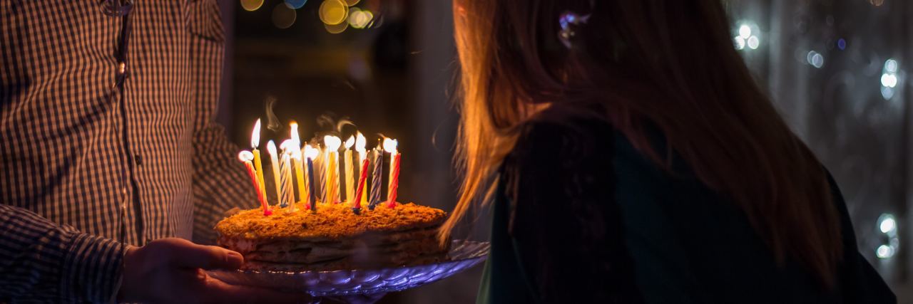 Lessons I Have Learned Approaching My 30s With PTSD woman blowing out birthday candles on cake held by man
