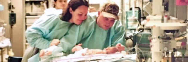 Mother and father leaning over tiny baby at hospital. Parents wear green paper hospital gowns.