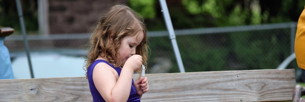 To the 'Exceptional Needs' Teacher Who Changed My Daughter's Life Little girl sitting on park bench, wearing a fancy purple dress, no shoes, and blowing bubbles