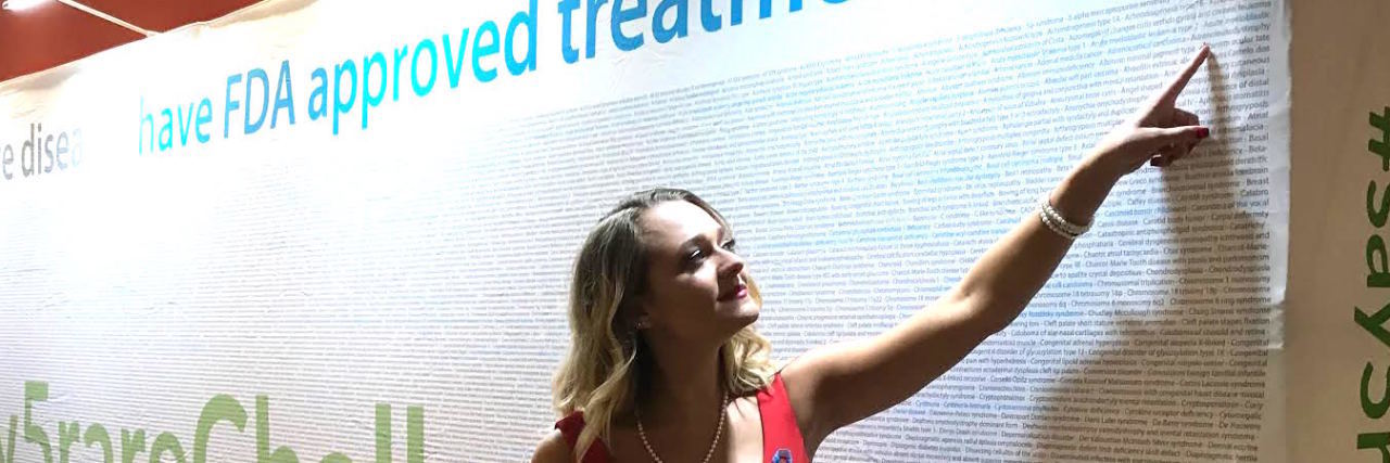 Being a Female Carrier of Adrenoleukodystrophy The author pointing to "adrenoleukodystrophy" on a wall about rare diseases