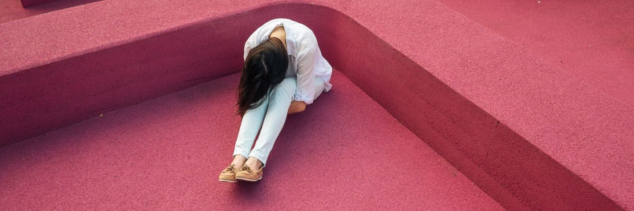 a woman sits on a pink floor hugging her legs to her chest