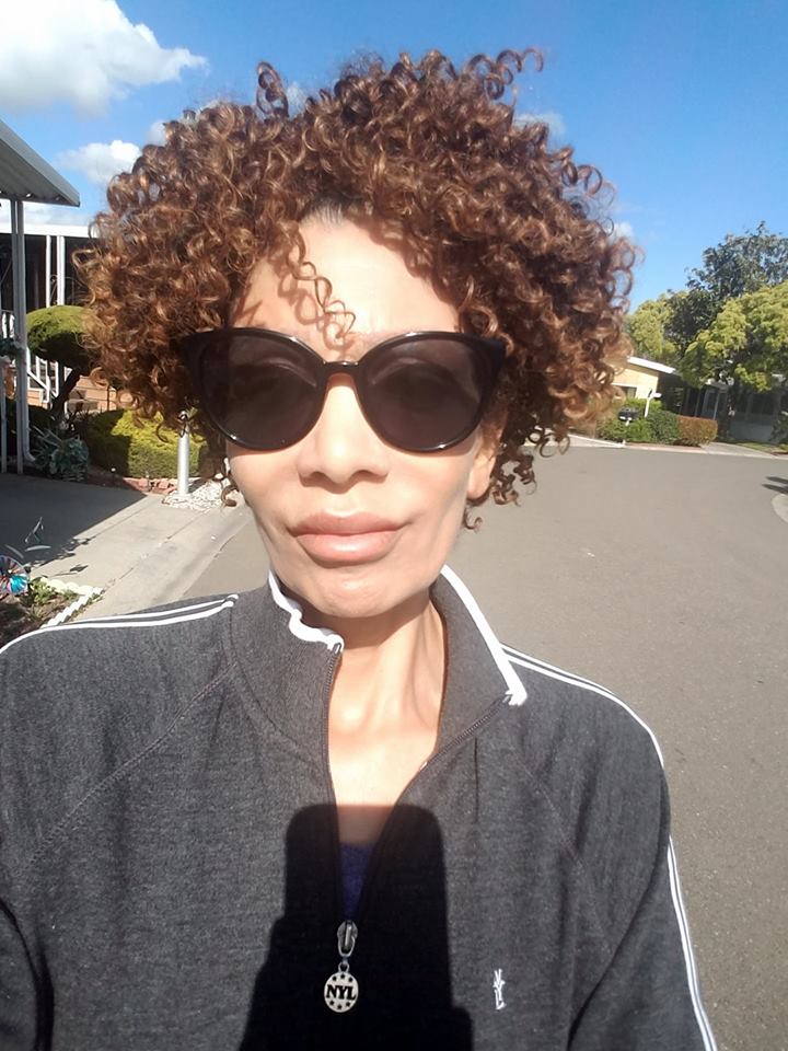 woman walking outside wearing a gray sweater and sunglasses