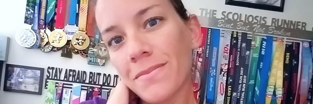 What It's Like to Have a Fibromyalgia Flare-Up the author wearing her purple 26.2 shirt and standing in front of a wall of medals