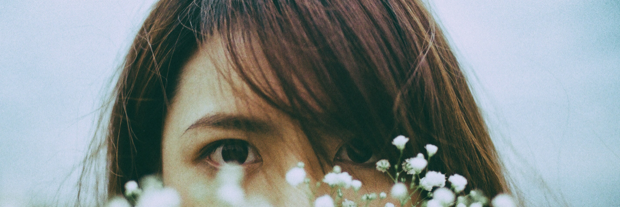 asian woman hiding behind flowers with eyes looking out over flowers