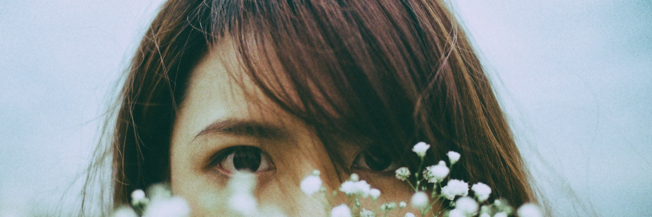 What People Wish They Knew Before Getting Diagnosed With Anxiety asian woman hiding behind flowers with eyes looking out over flowers