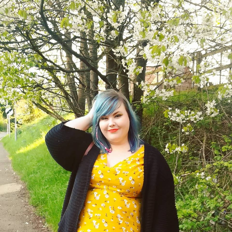 woman with blue hair standing outside and wearing a yellow dress and black jacket