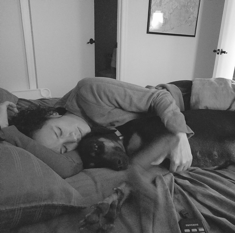 black and white photo of a woman lying in bed hugging her service dog