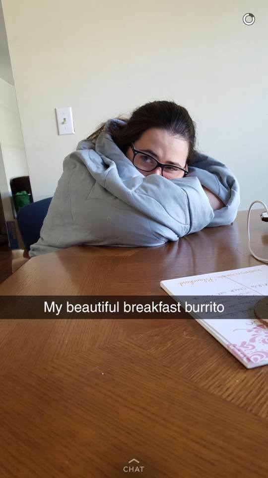 woman sitting at a table holding a blue blanket around her with the caption 'my beautiful breakfast burrito'