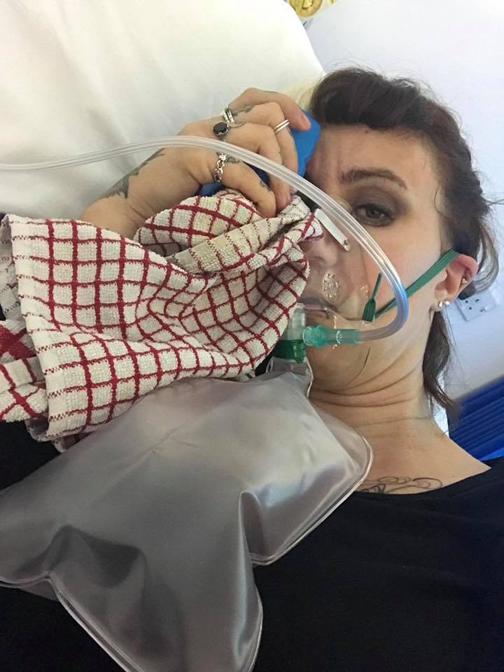 woman lying in a hospital bed wearing an oxygen mask and holding a rag