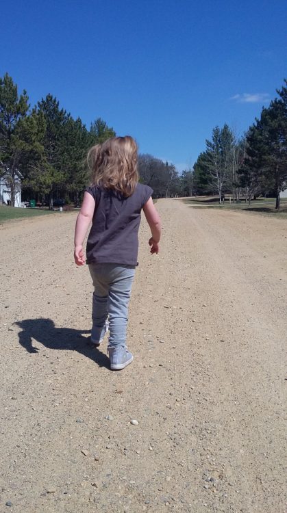 Back of little girl with Down syndrome walking down a dirt road