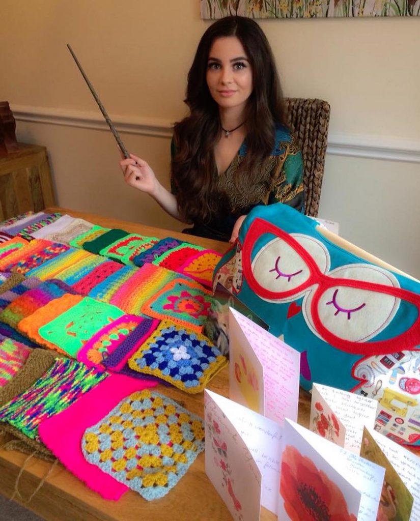 woman sitting at a table covered in colorful knitting squares