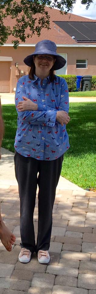 woman standing outside wearing black pants, a blue long-sleeve shirt and a wide-brimmed blue hat