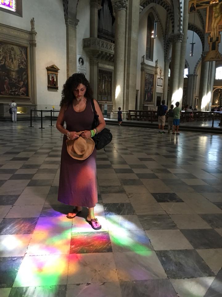 woman standing indoors looking at a rainbow of light reflected on the floor