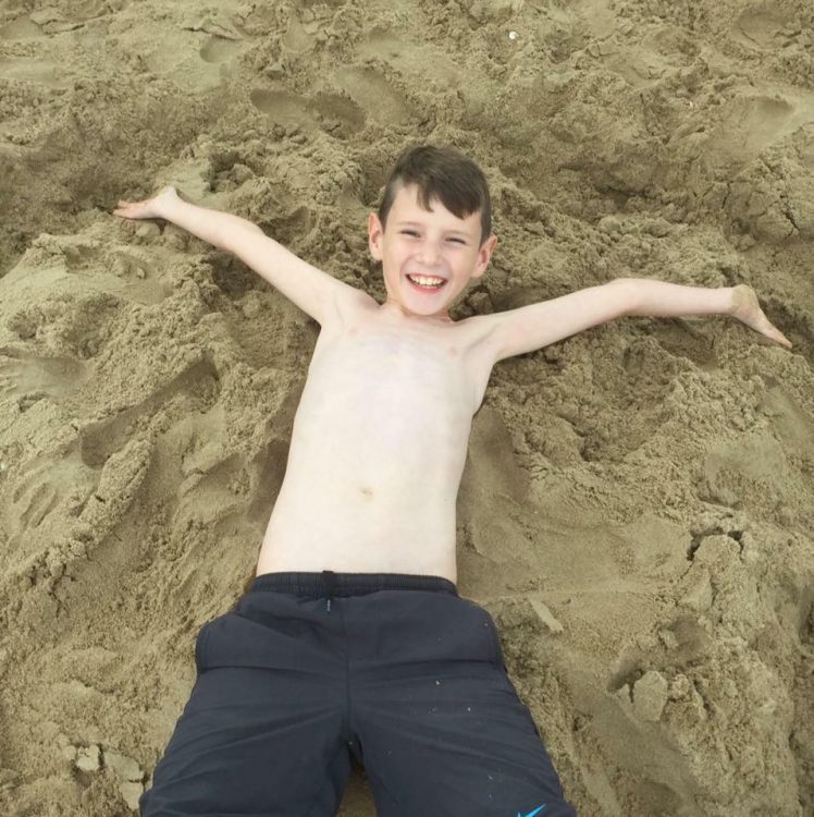 Jayne's son stretching his arms backwards in the sand