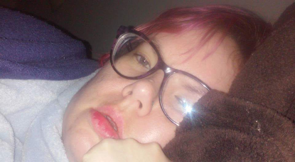 woman with short pink hair and glasses lying in bed