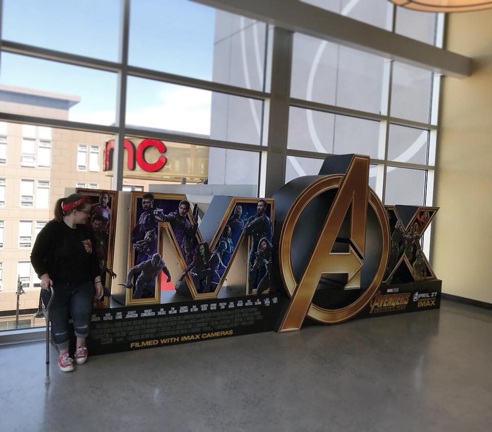 woman standing in front of an Avengers sign at a movie theater with her cane