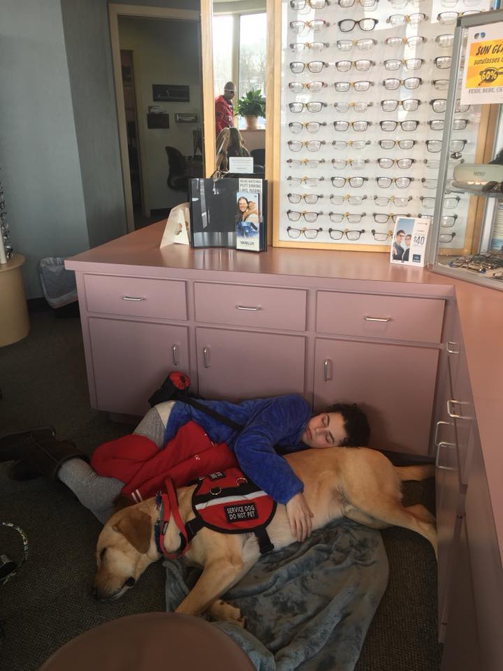 woman lying on the floor of a waiting room with her service dog