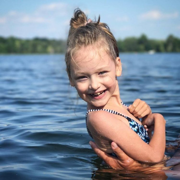 Little girl with cerebral palsy smiling in the middle of a lake, parent hands hold her up.