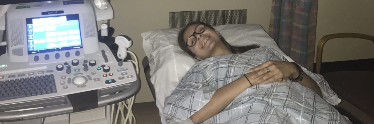 woman wearing glasses and lying in a hospital bed under a blanket