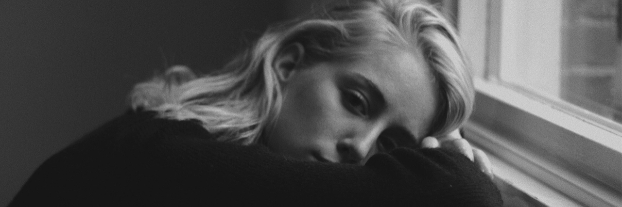 black and white photo of young woman leaning on windowsill depression