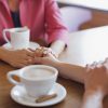 Woman holding hands over table, while having coffee together.
