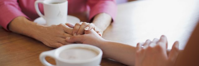 Woman holding hands over table, while having coffee together.