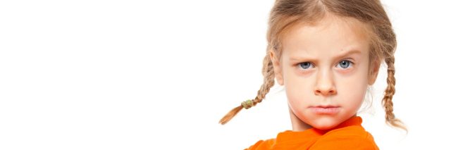 Little girl with pigtails looking at camera making a face, somewhat angry or puzzled