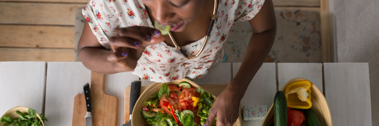 6 Healthy Cooking Tips for the Chronically Ill An African American woman eating a salad at a table, with the camera looking down at her.