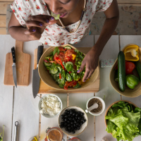 An African American woman eating a salad at a table, with the camera looking down at her.